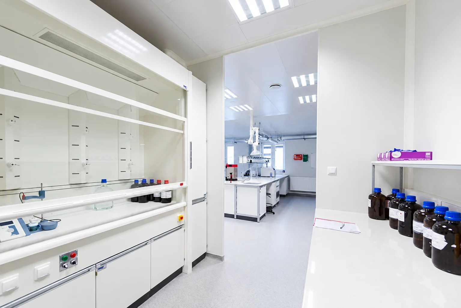 Abzüge mit Reagenzienregalen und ein Tisch mit Chemikalienflaschen im Labor